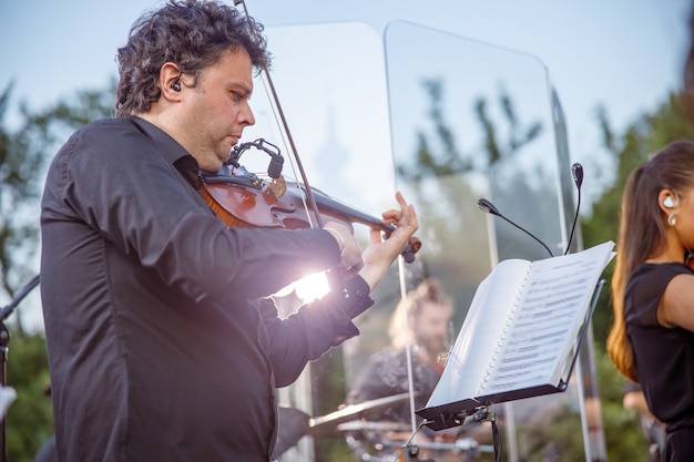 Serieuze man-muzikant die naar een muzikaal notitieboekje met notities kijkt en buiten viool speelt