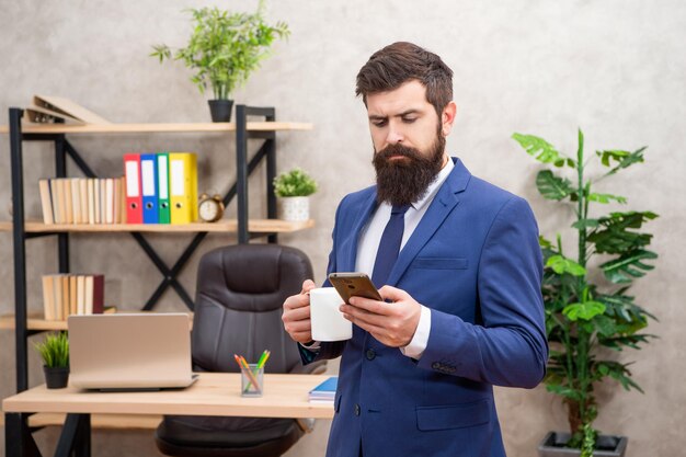 Serieuze manager in pak koffie drinken tijdens het lezen van sms op smartphone in office SMS