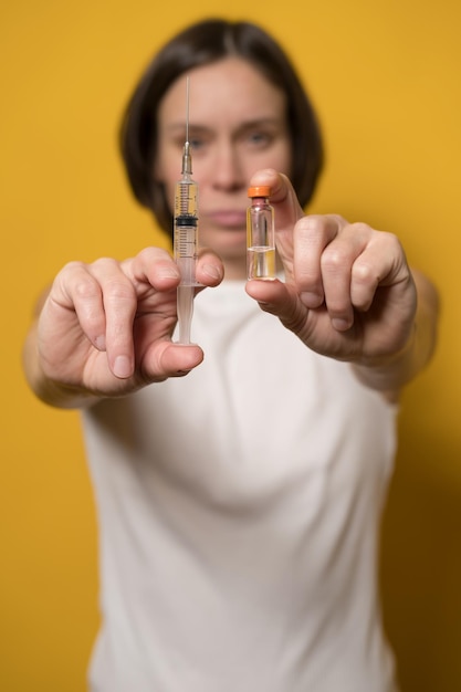 Serieuze vrouw houdt een spuit gevuld met vloeistof en een fles vaccin in haar hand