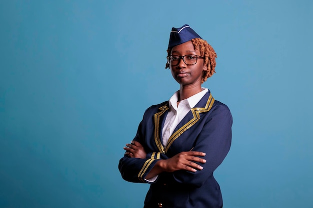 Serieuze vrouwelijke afro-amerikaanse stewardess analyseert opties voor aanstaande vluchtroutes op het werk. Stewardess dragen uniform in studio opname tegen blauwe achtergrond.