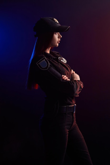 Serieuze vrouwelijke politieagent poseert voor de camera tegen een zwarte achtergrond met rode en blauwe ...