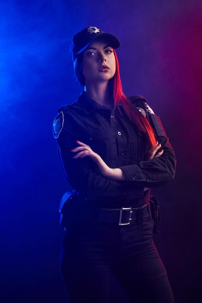 Serieuze vrouwelijke politieagent poseert voor de camera tegen een zwarte achtergrond met rode en blauwe ...
