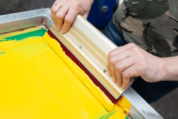 Serigraphy silk screen print process at clothes factory frame squeegee and plastisol color paints