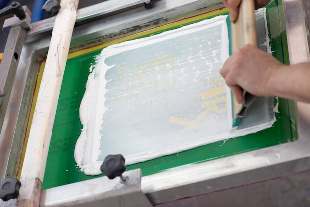 洋服工場でのセリグラフィーシルクスクリーン印刷工程 フレームスキージとプラスチゾルカラー塗料