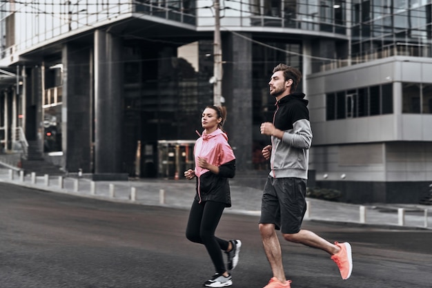 Serious about staying in shape. Full length of young couple in sport clothing running through the city street together