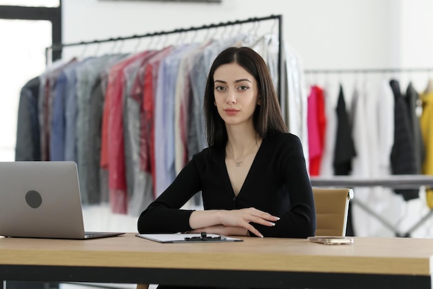 Serious administrator of dry cleaning sits at table near open laptop young brunette woman looks