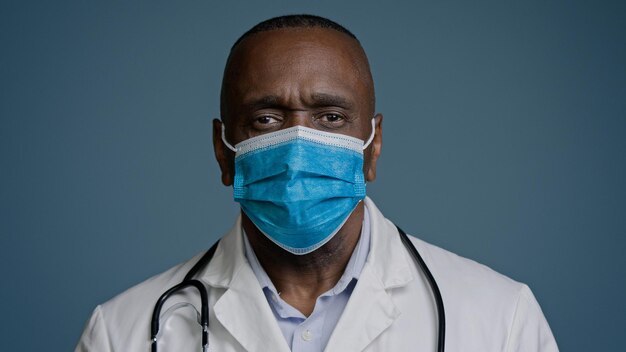 Serious african american mature man doctor surgeon therapist in medical gown and protective mask