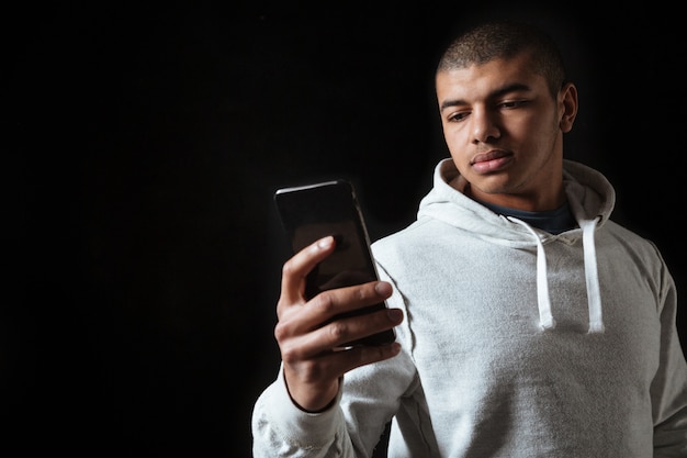 Serious african man in hoodie standing and using cell phone