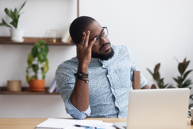 serious african millennial businessman thinking cogitating about business issues frustrated black entrepreneur searching problem solution sitting alone on chair at modern office desk looking away