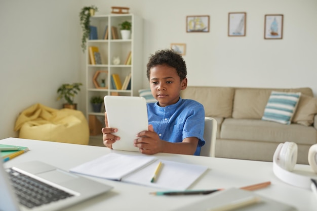 Photo serious africanamerican boy with curly hair sitting at desk in living room and watching educational