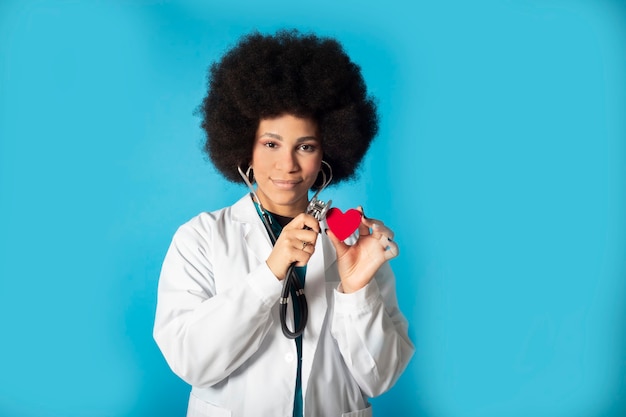 Serious afro woman holds with her hands a paper heart while winged holds a stotocope