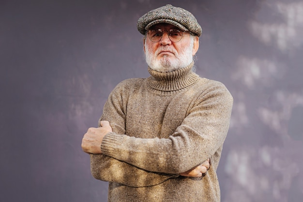 Фото Серьезный пожилой мужчина. уверенный в себе пожилой мужчина в стильном вязаном свитере и кепке, скрещивающей руки