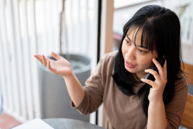 深刻なアジア人女性がカフェに座って誰かと電話で話している