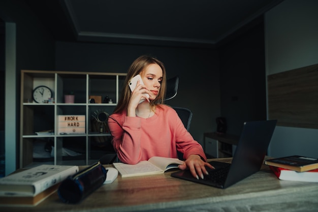 Serious attractive woman sitting at home at work and using a laptop and talking on the phone