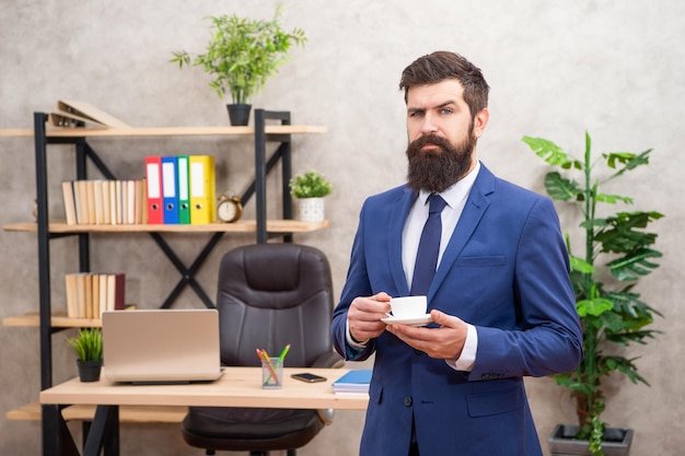 Серьезный бородатый бизнесмен пьет кофе в офисе с копировальным пространством