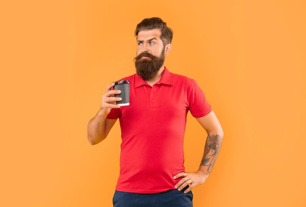 Serious bearded man in casual tshirt holding coffee cup with arm akimbo yellow background takeaway