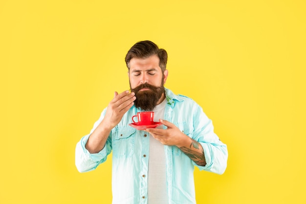 Serious bearded man drink morning coffee on yellow background coffee