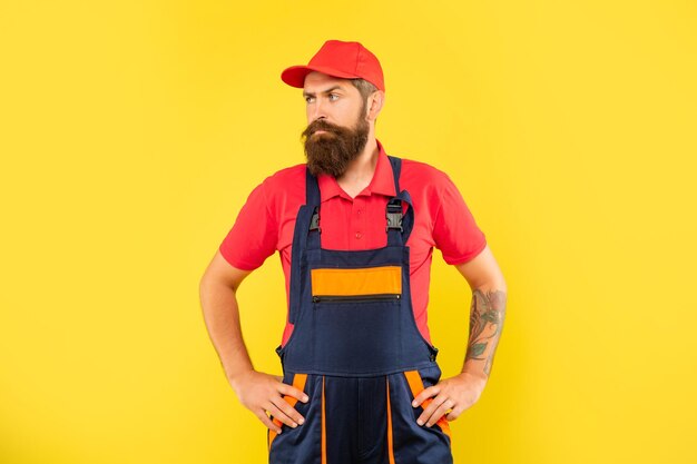 Serious bearded man loader in work clothes on yellow background