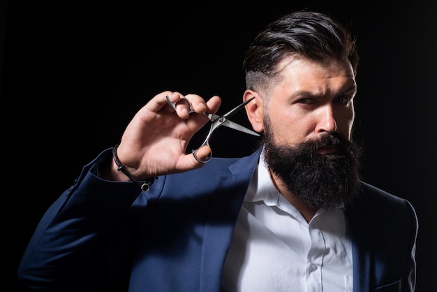 Serious bearded man, portrait of man with long beard and moustache. Barber scissors for barber shop. Vintage barbershop, shaving. Brutal serious male with modern hairstyle on black.