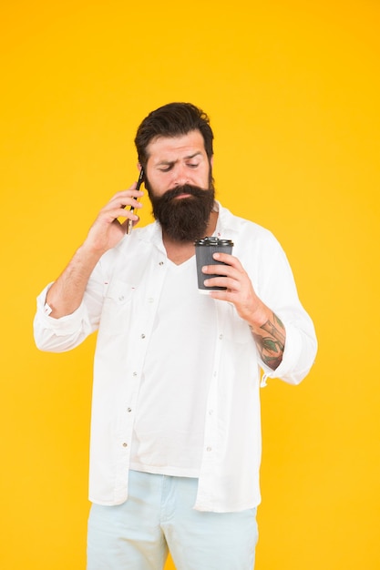 Серьезный бородатый мужчина разговаривает по телефону, пока пьет утренний кофе