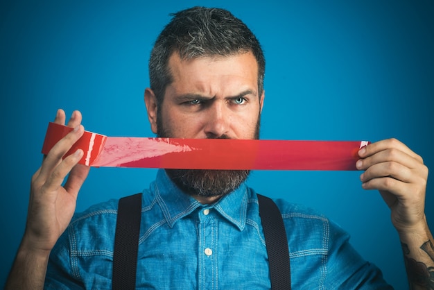 Serious bearded worker with mouth covered by red adhesive tape\
casual man wrapping duct tape over
