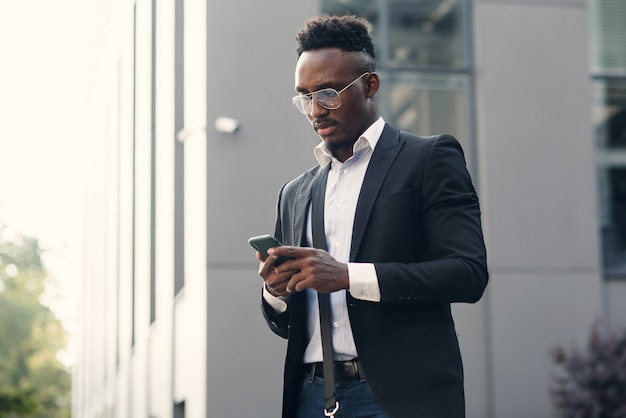 Серьезный черный бизнесмен текстовых сообщений на смартфоне на открытом воздухе