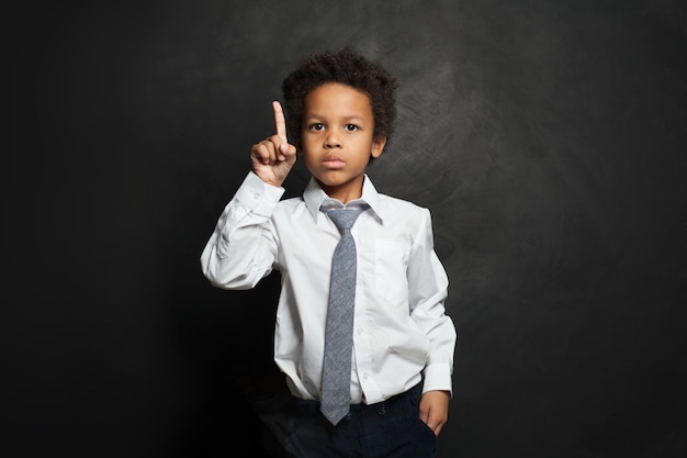 真剣な黒い子供黒い肖像画を指差している学生の男の子