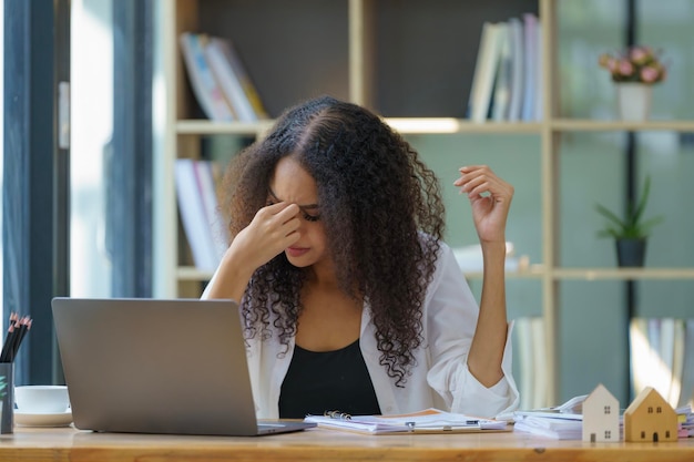 serious black woman entrepreneur using a laptop and reading documents while planning the companys budget and working through financial papers in her office