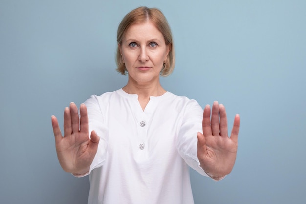 Serious blond bob middle aged woman in white blouse in menopause refuses on studio background