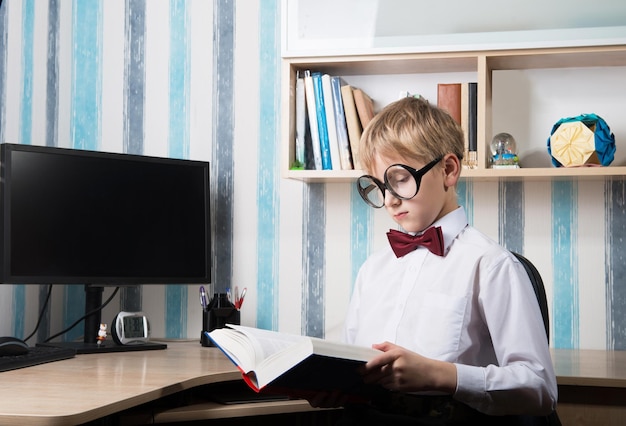 Serious boy in the bow tie reading a book at home