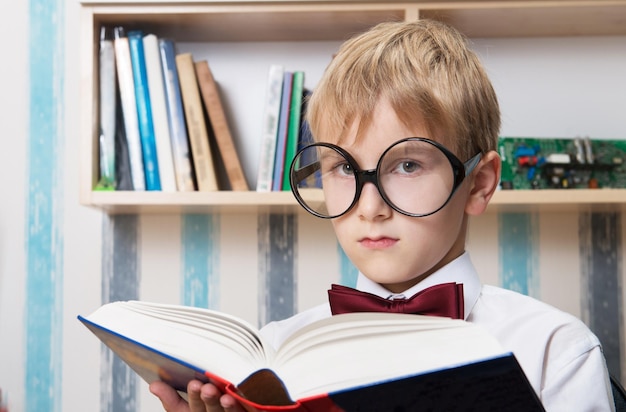 Serious boy in the bow tie reading a book at home