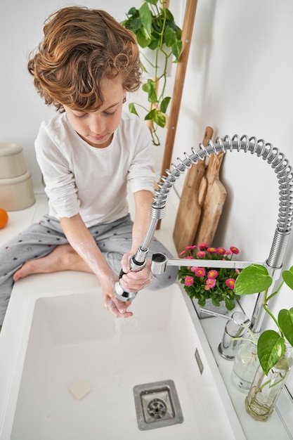 Serious boy washing hands with soap and clear water