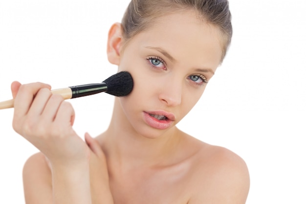 Serious brunette model applying powder on her cheek