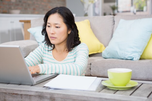 Serious brunette using laptop in the living room