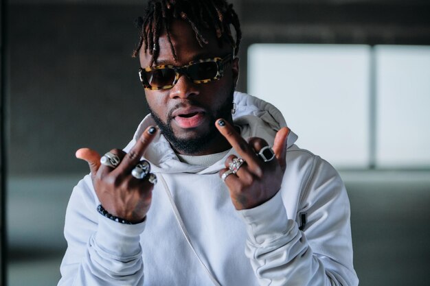 Photo serious brutal male in trendy white outfit and sunglasses showing middle finger gestures to camera