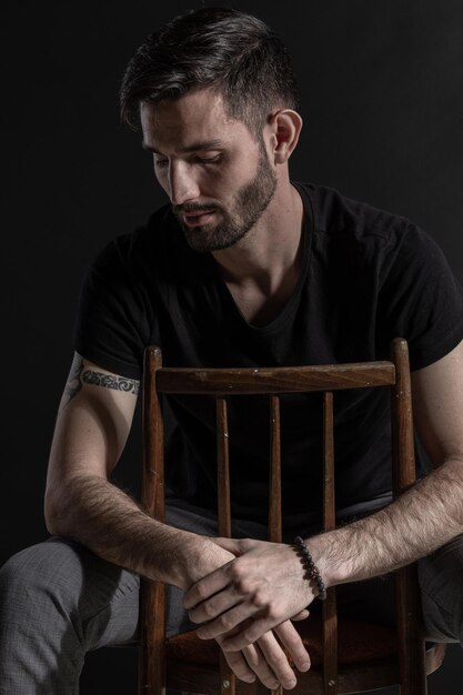 Serious brutal man with tattoo and beard posing on the chair on the black background