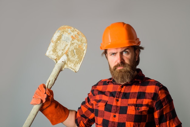 Серьезный строитель в каске с лопатой рекламирует ремонтника с лопатой в работе
