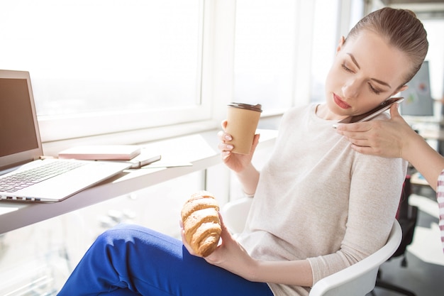 Foto donna seria di affari che parla al telefono e che mangia prima colazione