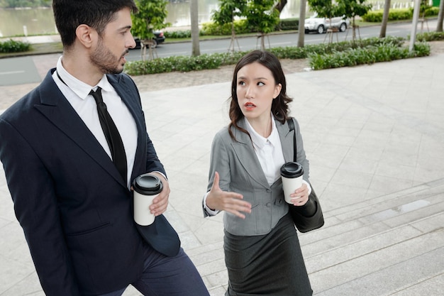 Серьезные коллеги по бизнесу гуляют на свежем воздухе, пьют утренний кофе и обсуждают работу