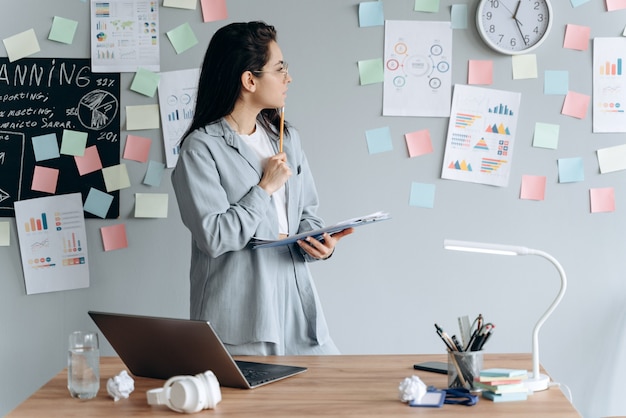 A serious, business girl is carefully studying a chart hanging on the wall