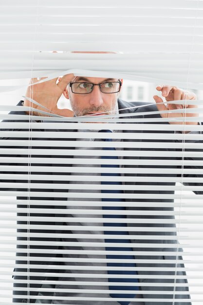 Serious businessman peeking through blinds in office