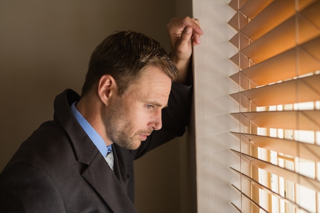 Serious businessman peeking through blinds