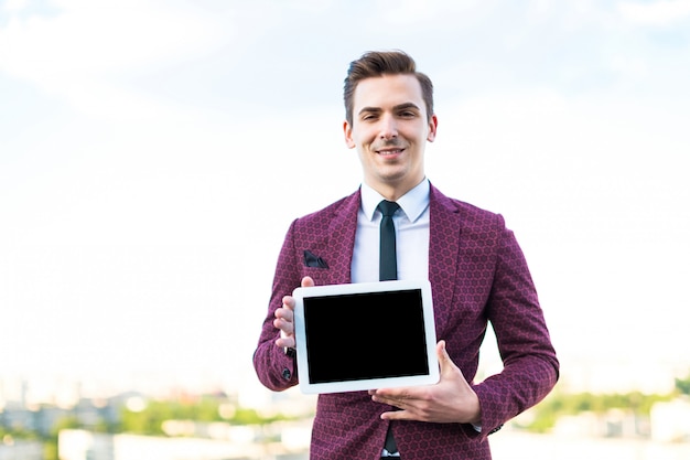 Serious businessman in red suit and shirt with tie stand on the roof with empty tablet