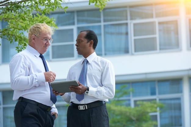 Serious businessman showing tablet computer to colleague