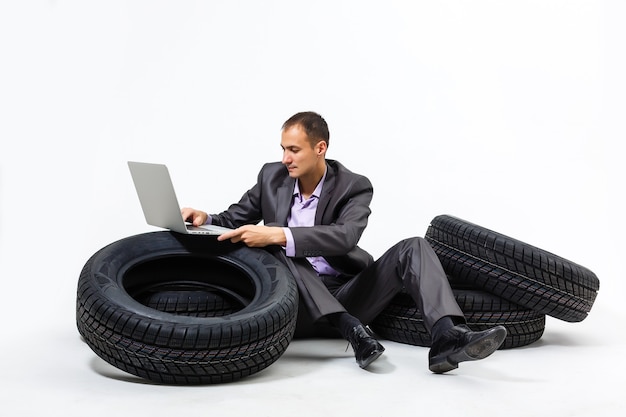 A serious businessman sitting on a stack of car tires. Repair shop. Car service. Spare parts reselling. solated on white background