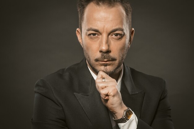 Serious Businessman touches the chin on grey background. Portrait of a successful confidence man in elegant formalwear looking at the camera.