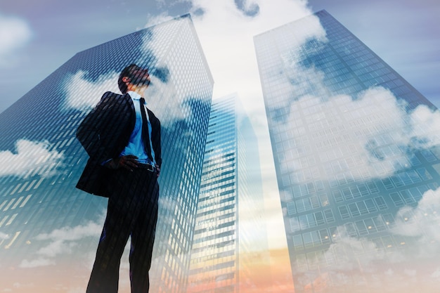 Serious businessman with hands on hips against low angle view of skyscrapers