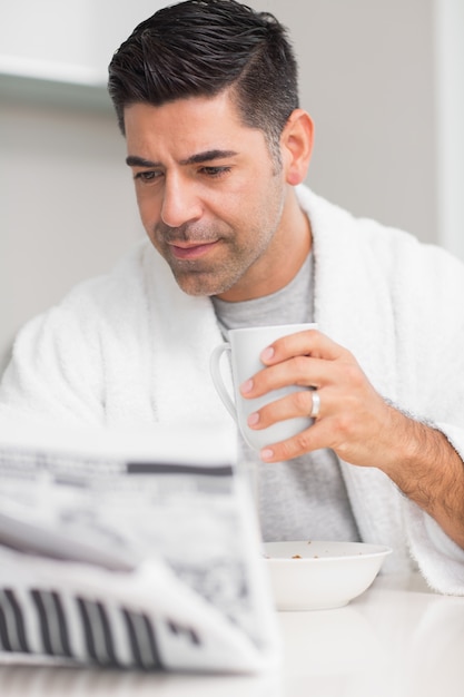 Serious casual man with coffee cup reading newspaper