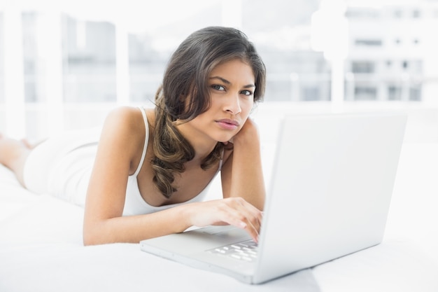 Serious casual woman using laptop in bed