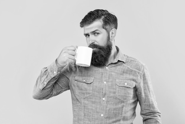 Serious caucasian guy drinking coffee from mug yellow background